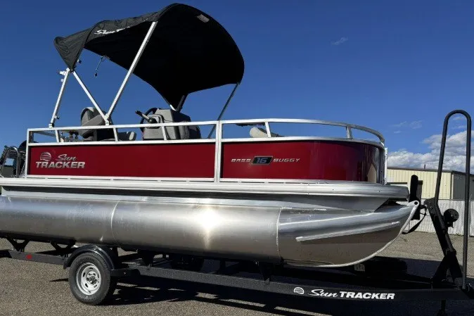 The Image of 2026 Sun Tracker Bass Buggy 16 XL Select pontoon boat on trailer, under clear blue sky. - 0