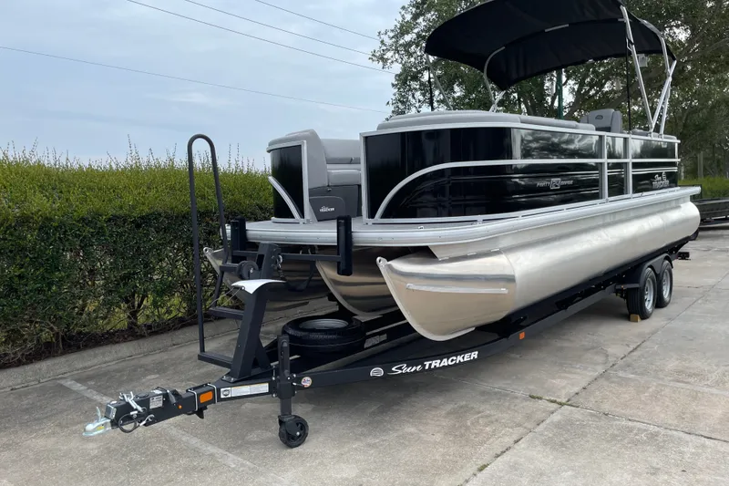 Slide: The Image of 2026 Sun Tracker Party Barge 24 XP3 pontoon boat on trailer, parked outdoors. - 2