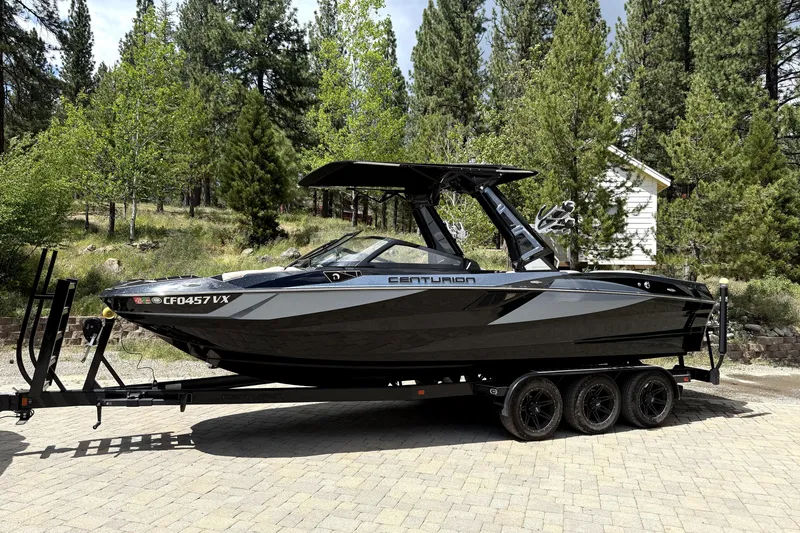 The Image of 2023 Centurion Fi25 boat on trailer, surrounded by lush green trees. - 1