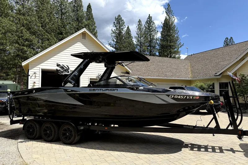 Slide: The Image of 2023 Centurion Fi25 boat on trailer in driveway, surrounded by trees and house. - 2
