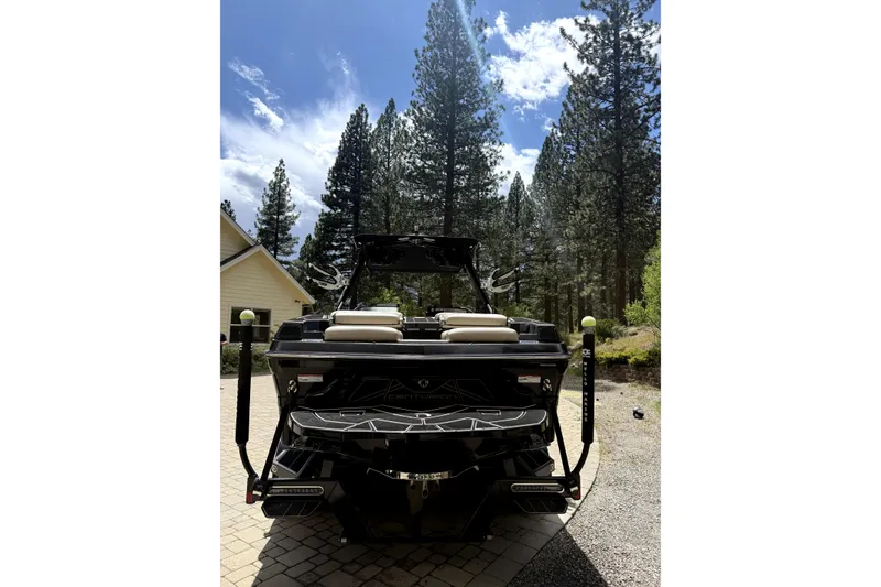 Slide: The Image of 2023 Centurion Fi25 boat parked on a driveway, surrounded by tall pine trees. - 6
