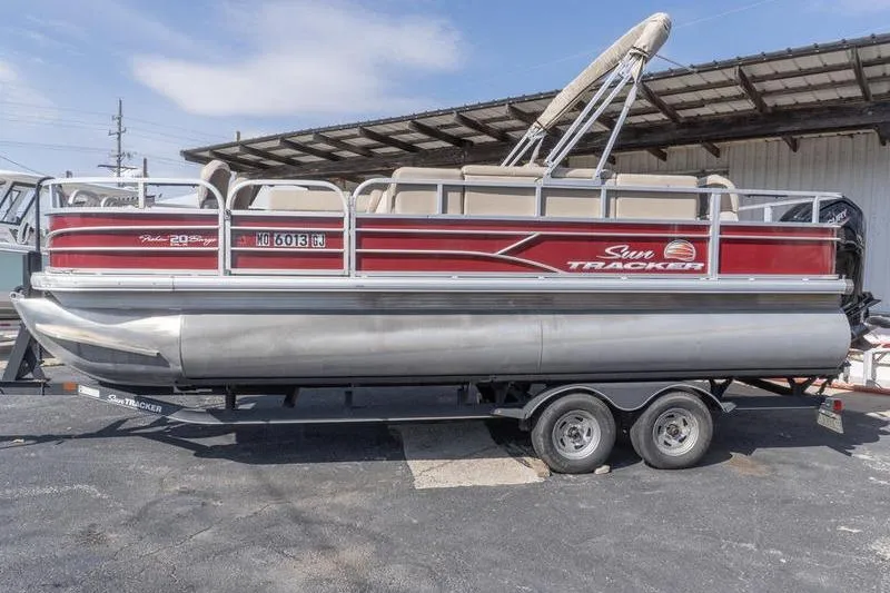 Slide: The Image of 2019 Sun Tracker Fishin' Barge 22 DLX pontoon boat on trailer, parked outdoors. - 2