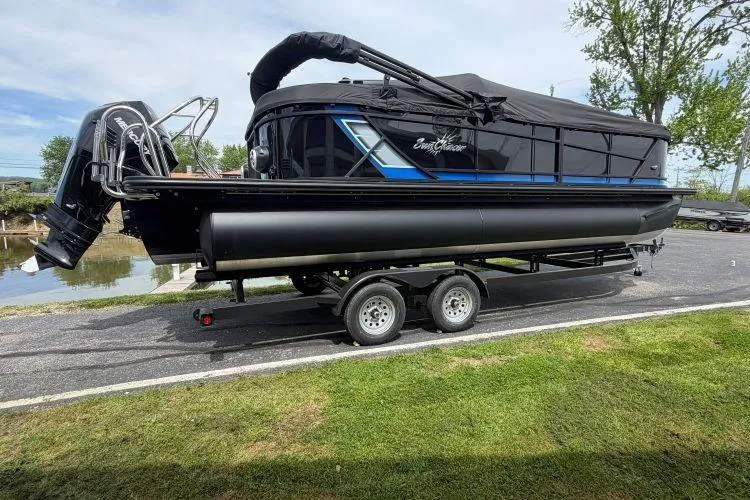 The Image of 2026 SunChaser Geneva Sport 23 LR DH pontoon boat on trailer, black exterior, parked near water. - 0