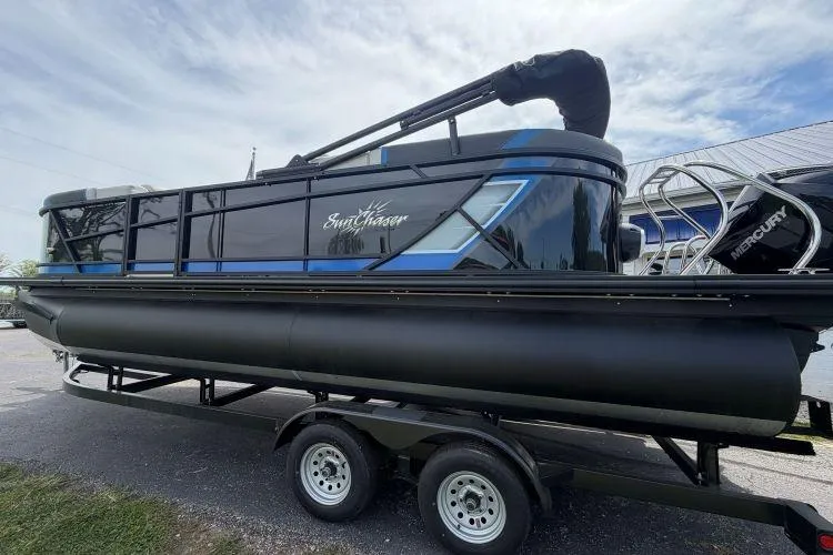 Slide: The Image of 2026 SunChaser Geneva Sport 23 LR DH pontoon boat on trailer, featuring sleek black and blue design. - 2