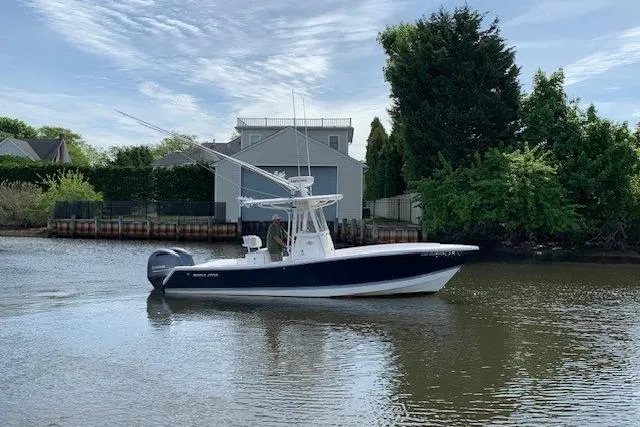Slide: The Image of 2006 Regulator 24 Classic boat on calm water, surrounded by lush greenery and houses. - 21
