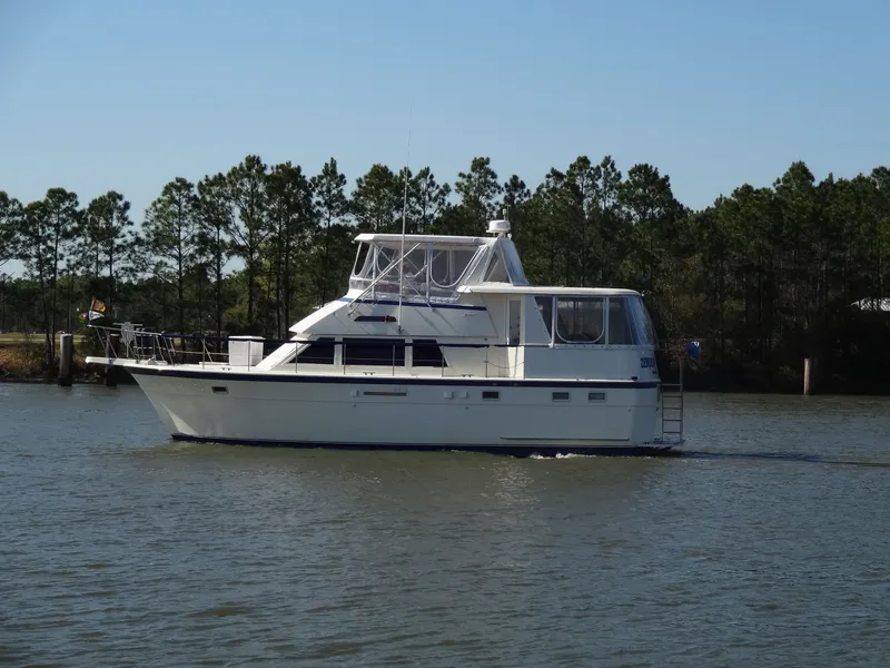 Slide: The Image of 1987 Hatteras 43 yacht cruising on calm water near trees. - 10
