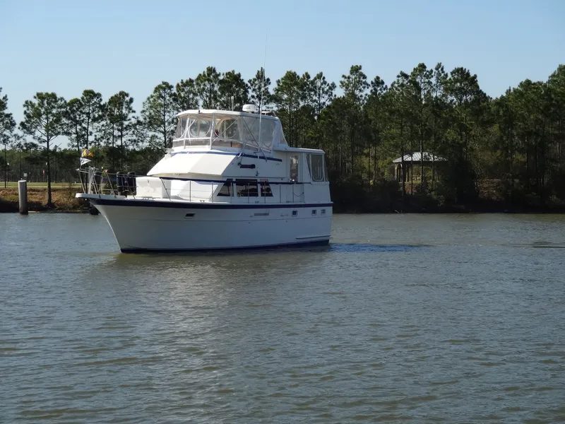 Slide: The Image of 1987 Hatteras 43 yacht cruising on calm water near trees. - 12