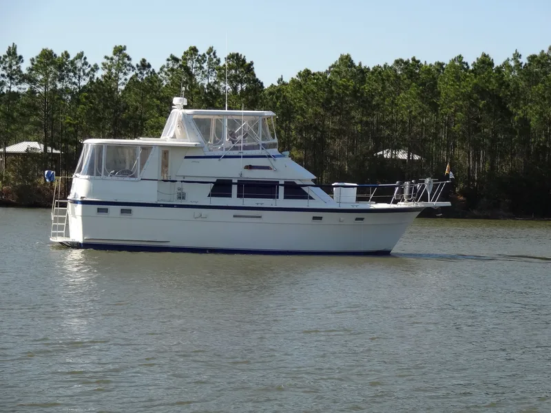 Slide: The Image of 1987 Hatteras 43 yacht cruising on calm water with forest backdrop. - 19