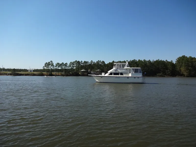 Slide: The Image of 1987 Hatteras 43 yacht on calm water with forest backdrop. - 8