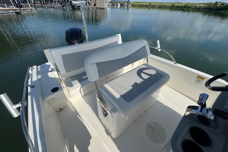 Slide: The Image of 2014 Boston Whaler 210 Dauntless boat interior with seating and steering wheel, docked on calm water. - 25