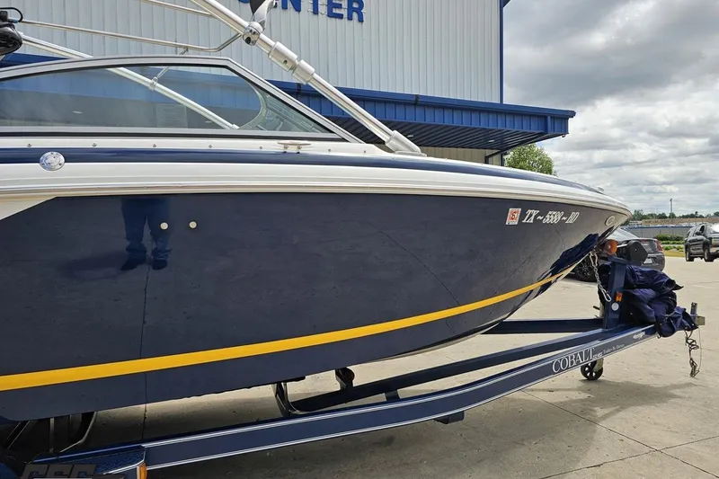 Slide: The Image of 2010 Cobalt 232 WSS boat on trailer, parked outside a building under cloudy skies. - 11