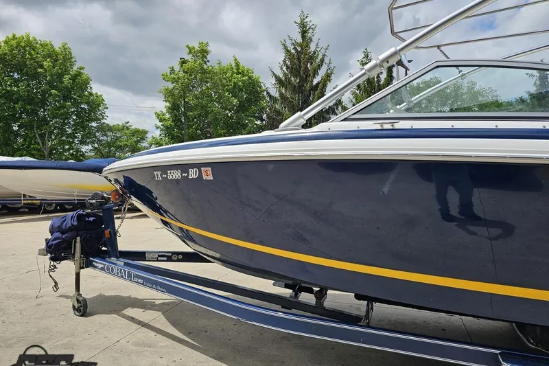 Slide: The Image of 2010 Cobalt 232 WSS boat on trailer, parked outdoors with trees in background. - 23