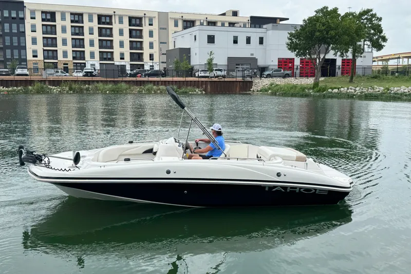 The Image of 2017 Tahoe 195 boat cruising on a calm river near urban buildings. - 1