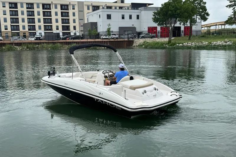 Slide: The Image of 2017 Tahoe 195 boat cruising on a calm river near modern buildings. - 3