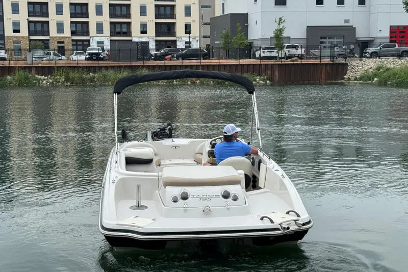 Slide: The Image of Man steering a 2017 Tahoe 195 boat on a calm river near urban buildings. - 4