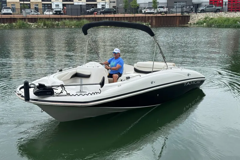 Slide: The Image of 2017 Tahoe 195 boat on water with a person steering, urban backdrop. - 8