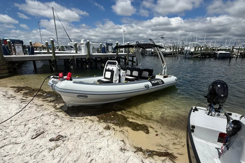 Slide: The Image of 2026 Highfield Velox 560 boat docked on sandy shore near marina under cloudy sky. - 5