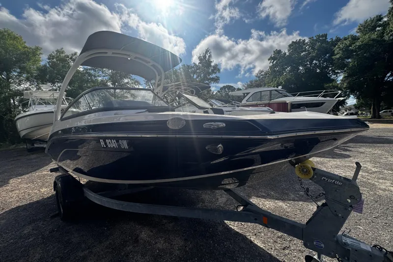 Slide: The Image of 2021 Yamaha Boats 195S on trailer under sunny sky, surrounded by trees and other boats. - 8