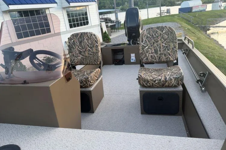 Slide: The Image of 2026 Smoker Craft Sportsman 1660 boat interior with camo seats, steering wheel, and lake view. - 6