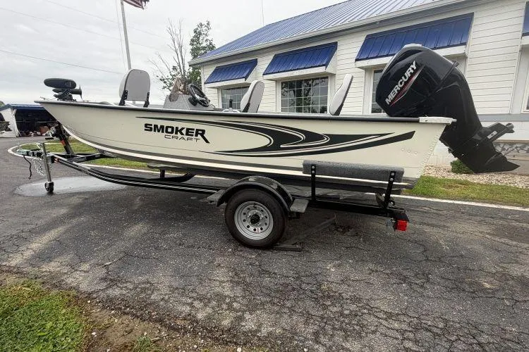 Slide: The Image of 2026 Smoker Craft Angler 16 SC boat on trailer, parked outdoors near a building. - 2
