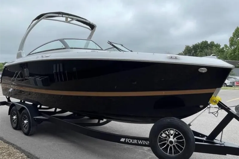 Slide: The Image of 2026 Four Winns H6 boat on trailer, sleek black design, parked outdoors. - 2