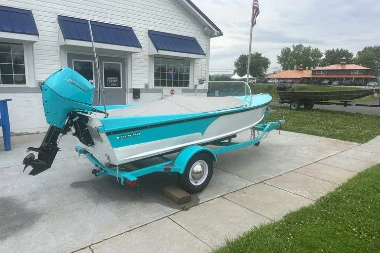 Slide: The Image of Turquoise and white 2026 Starcraft 57 Ski Champ boat on trailer outside a building. - 3