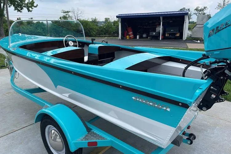 Slide: The Image of Turquoise 2026 Starcraft 57 Ski Champ boat on trailer, parked near a garage. - 5