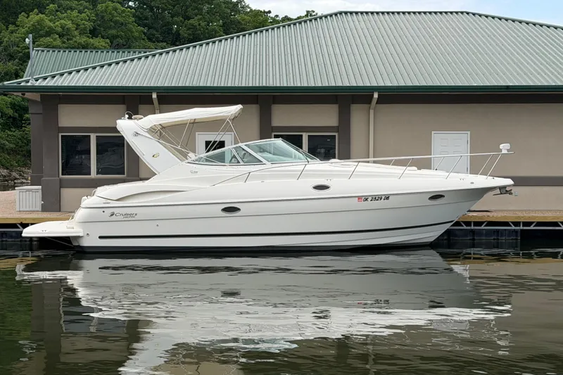 The Image of 2004 Cruisers Yachts 320 Express docked by a building, reflecting on calm water. - 1