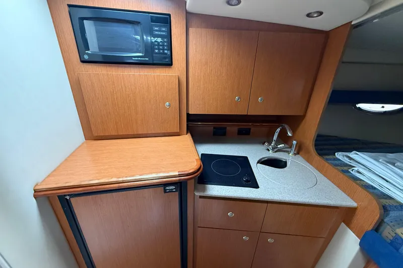 Slide: The Image of 2004 Cruisers Yachts 320 Express galley with microwave, stove, sink, and wood cabinetry. - 6