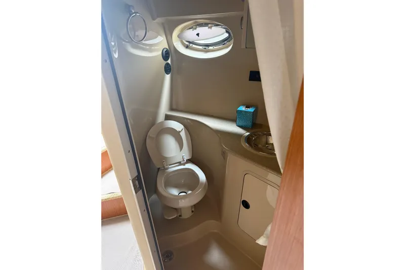 Slide: The Image of 2004 Cruisers Yachts 320 Express bathroom with toilet, sink, and porthole window. - 9