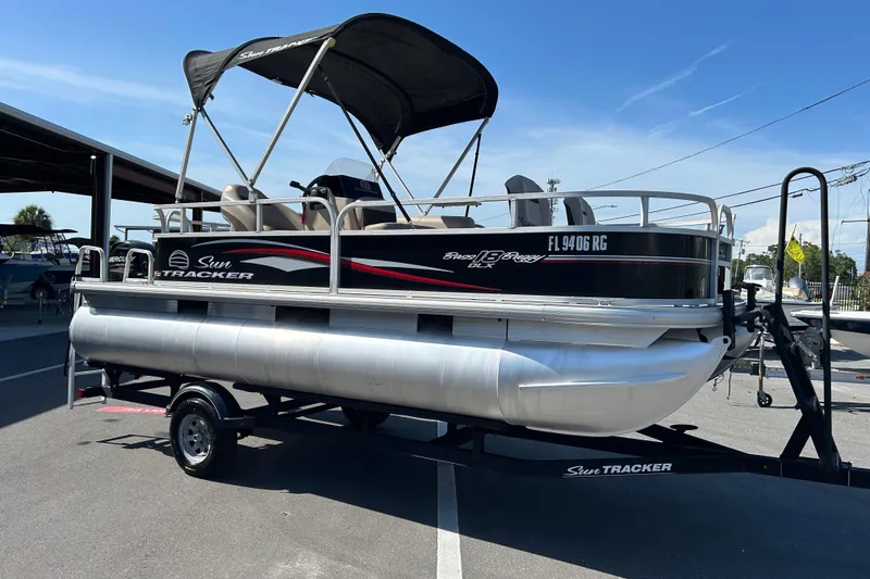 The Image of 2017 Sun Tracker Bass Buggy 18 DLX pontoon boat on trailer, under sunny sky. - 1