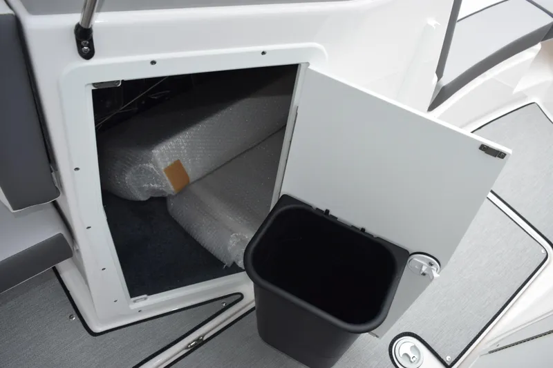 Slide: The Image of 2026 Yamaha Boats AR220 storage compartment with open door and black bin. - 17