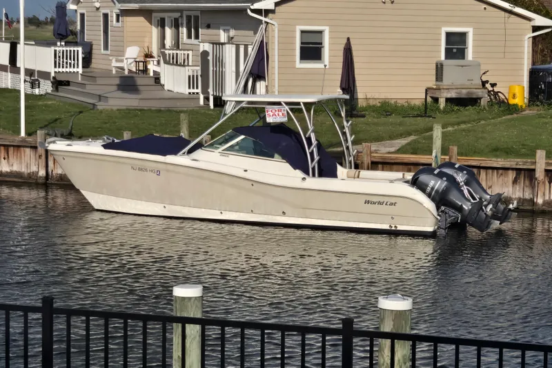 The Image of 2015 World Cat 295 DC boat docked, for sale sign visible, near waterfront home. - 0