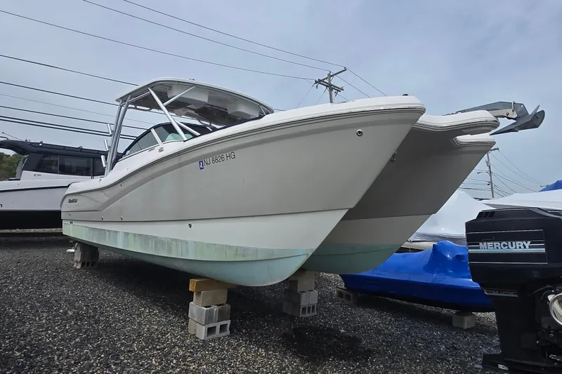 Slide: The Image of 2015 World Cat 295 DC boat on blocks, displayed outdoors with Mercury engine nearby. - 8