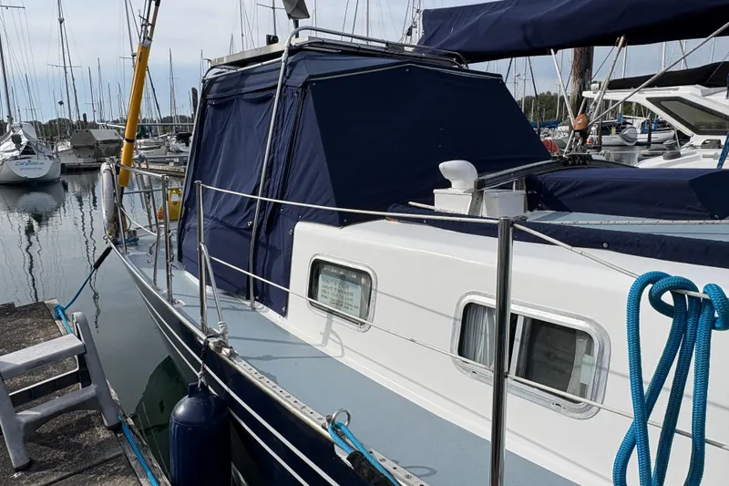 Slide: The Image of 1977 Folkes Full Keel Offshore Cutter docked at marina, featuring blue canopy and white hull. - 12