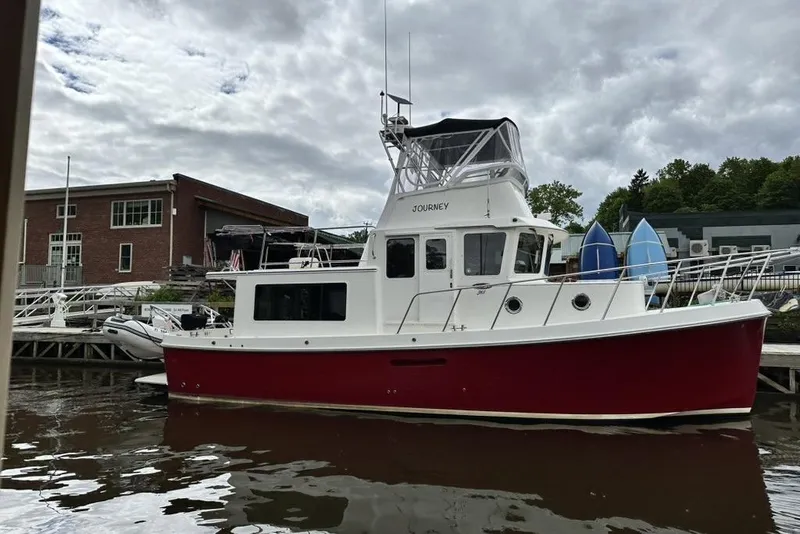 Slide: The Image of 2012 American Tug 365 Flybridge docked, featuring a red hull and flybridge under cloudy skies. - 113