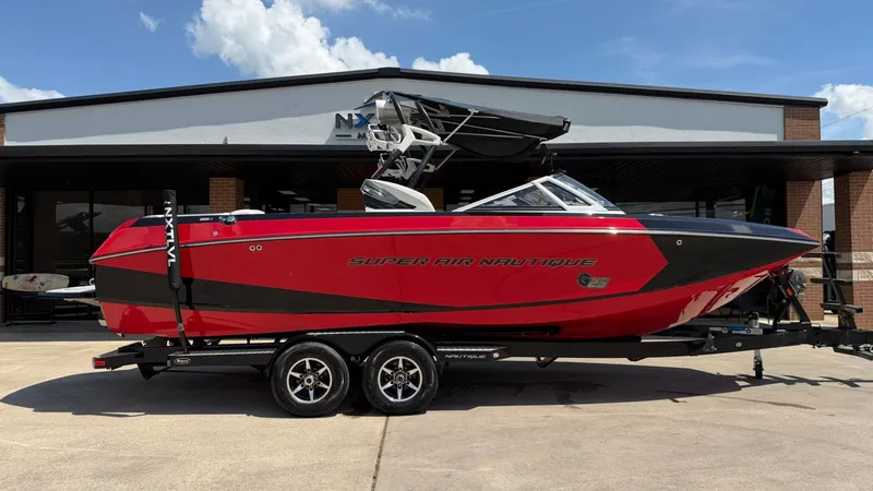 The Image of Red 2014 Nautique G25 boat on trailer in front of building. - 1