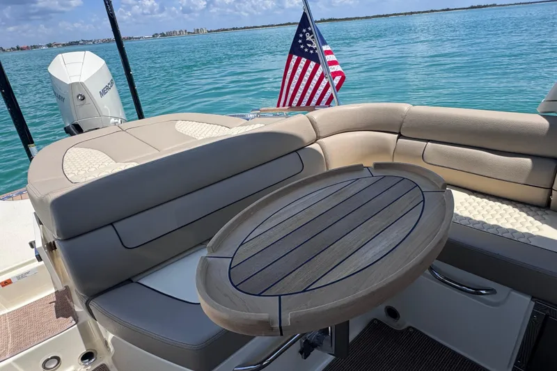 Slide: The Image of 2023 Chris-Craft Launch 25 GT boat interior with seating, table, and American flag on calm water. - 20