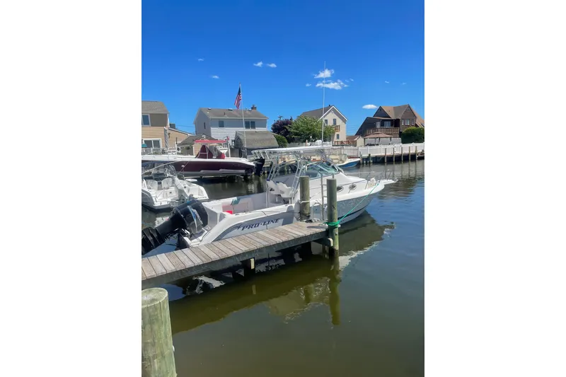 The Image of 2002 Pro-Line 260 Walkaround boat docked in a scenic marina under a clear blue sky. - 1