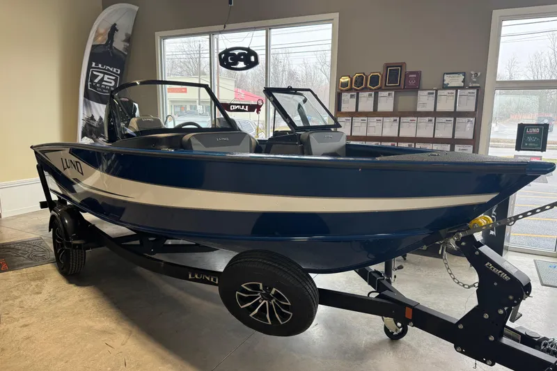 The Image of 2026 Lund 1875 Crossover XS boat in showroom, blue and white design, on trailer. - 0
