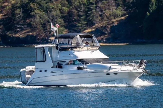 The Image of 1999 Sea Ray 420 Aft Cabin cruising on a scenic lake with forested backdrop. - 0