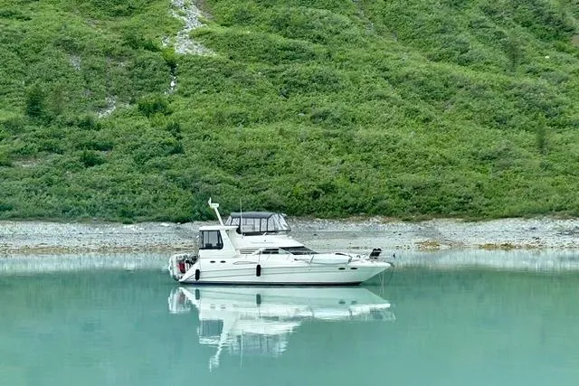 Slide: The Image of 1999 Sea Ray 420 Aft Cabin yacht on serene turquoise water, lush green backdrop. - 3