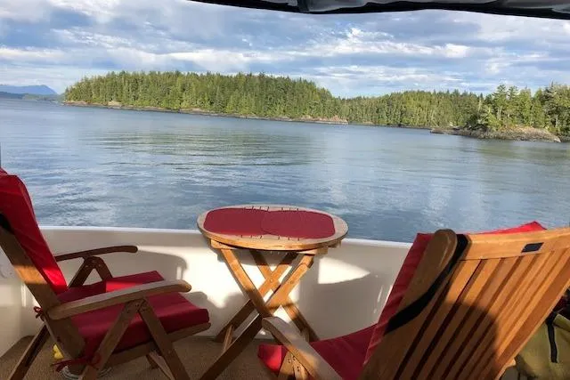 Slide: The Image of 1999 Sea Ray 420 Aft Cabin yacht with scenic lake view and wooden deck chairs. - 8