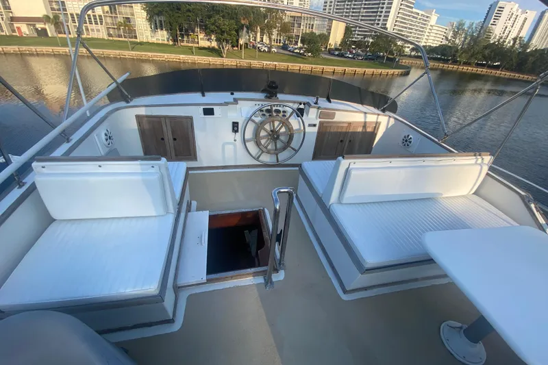 Slide: The Image of 1985 Marine Trader 50 Motor Yacht deck with seating and steering wheel, docked by waterfront. - 6
