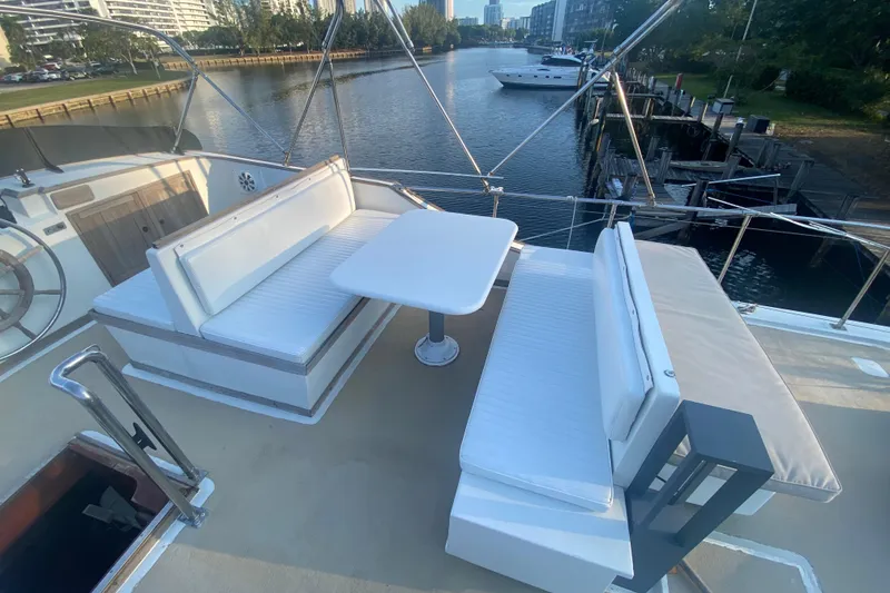 Slide: The Image of 1985 Marine Trader 50 Motor Yacht deck with seating and table, overlooking a serene waterway. - 7