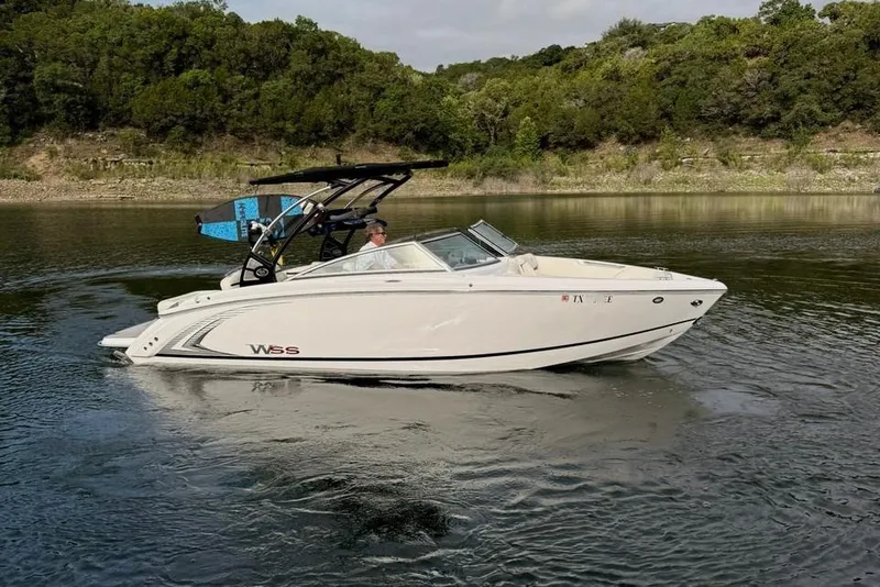 Slide: The Image of 2018 Cobalt R5 WSS Surf boat cruising on a serene lake with lush greenery. - 15
