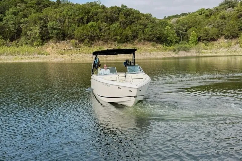 Slide: The Image of 2018 Cobalt R5 WSS Surf boat cruising on a serene lake with lush greenery. - 18