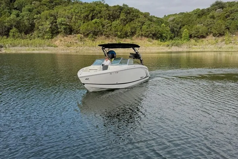 Slide: The Image of 2018 Cobalt R5 WSS Surf boat cruising on a serene lake with lush green surroundings. - 20