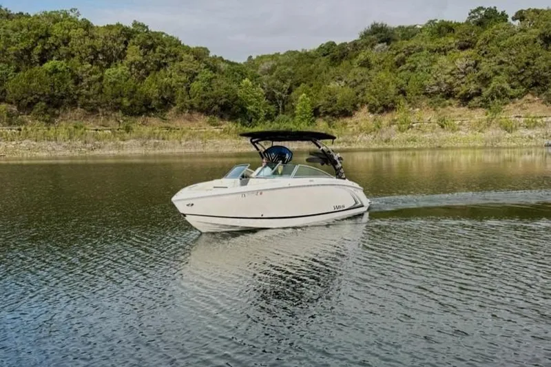 Slide: The Image of 2018 Cobalt R5 WSS Surf boat cruising on a serene lake with lush greenery. - 21
