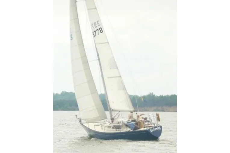 The Image of 1975 Carter 3/4 Ton sailboat on water, white sails, blue hull, distant shoreline. - 1